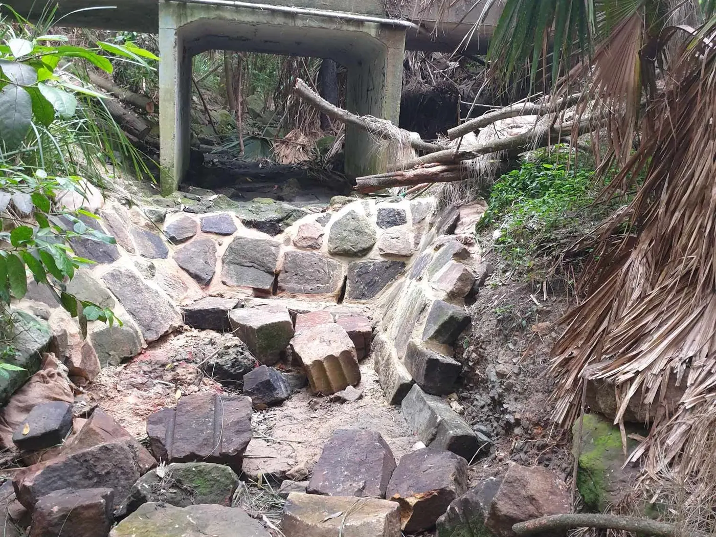 Completed stone-lined drainage channel beneath a bridge