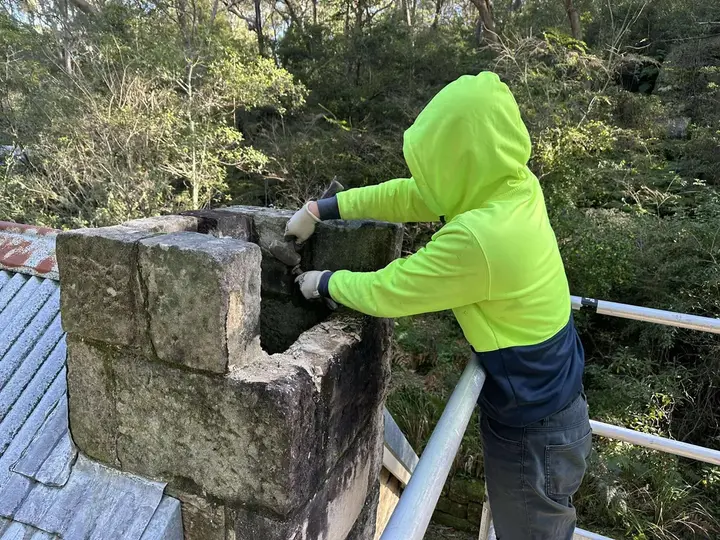 Stonemason rebuilding the upper courses of a heritage chimney